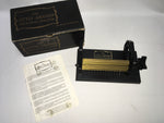 The image shows 'The Little Amanda Smocking Pleater' with its original box, instruction manual, and 12 needles. The pleater itself is black and gold in color.