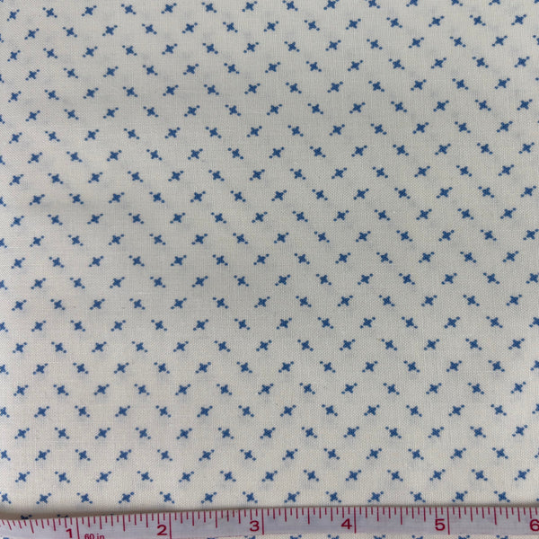 Fabric with blue cross pattern on a off-white background, measured with a ruler.